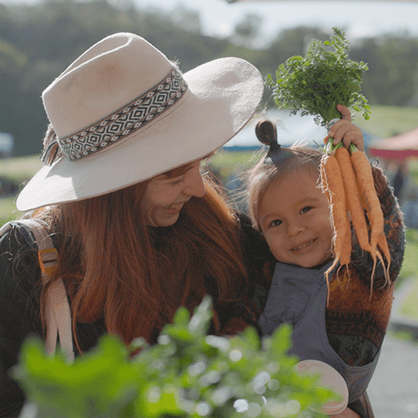 a woman holding a toddler who is holding a bunch of carrots