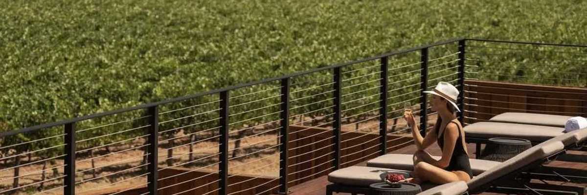 a woman in a bathing suit and hat on a pool deck overlooking vineyards