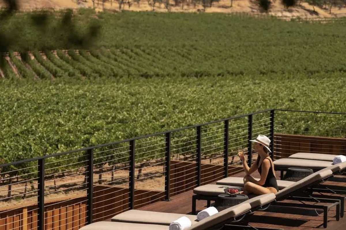 a woman in a bathing suit and hat on a pool deck overlooking vineyards