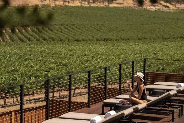 a woman in a bathing suit and hat on a pool deck overlooking vineyards