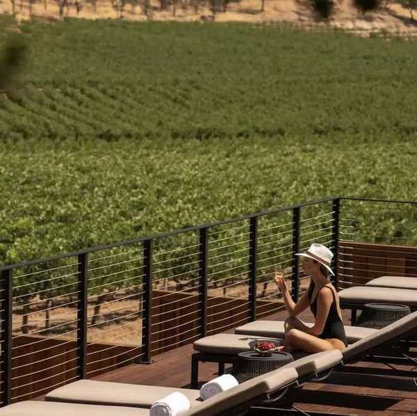 a woman in a bathing suit and hat on a pool deck overlooking vineyards