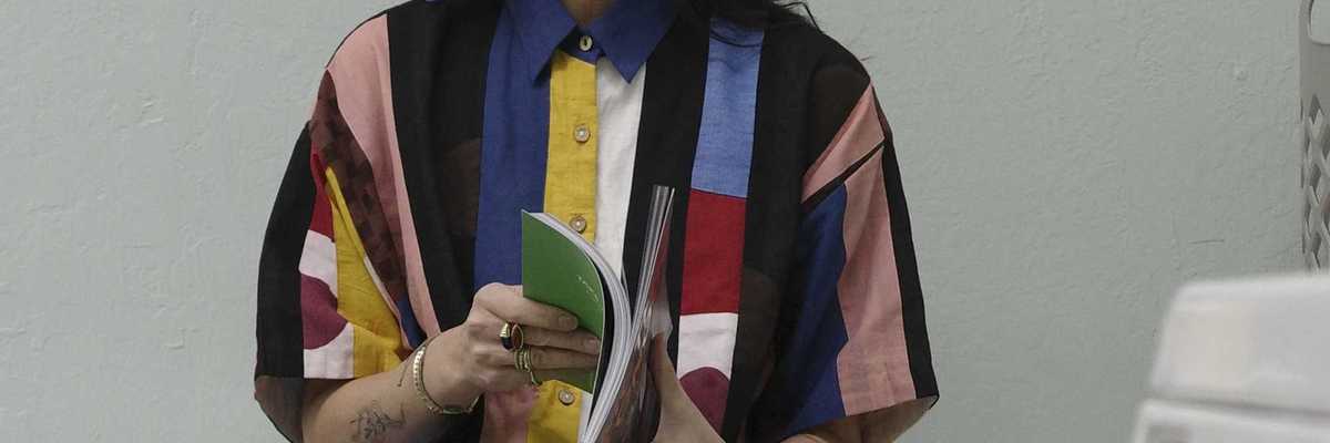 a woman in a colorful dress sitting ona washing machine and reading a book