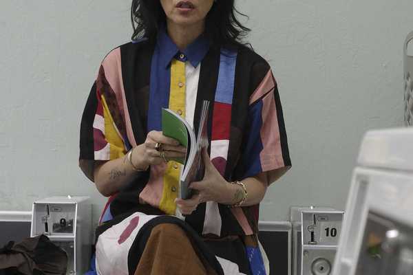 a woman in a colorful dress sitting ona washing machine and reading a book