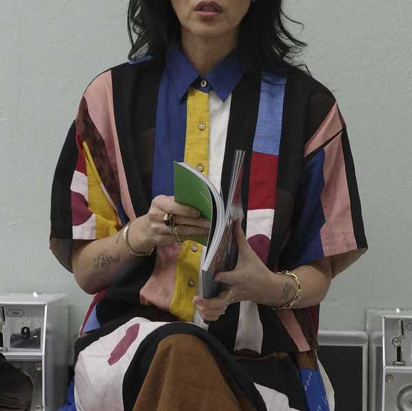 a woman in a colorful dress sitting ona washing machine and reading a book