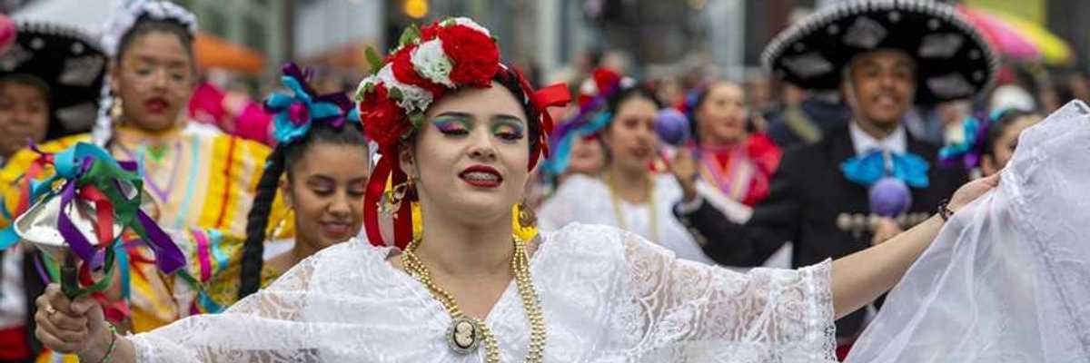 A woman in a traditional Mexican outfit with others in similar clothing parading behind her