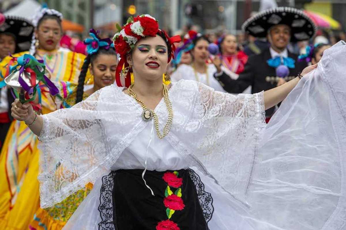 A woman in a traditional Mexican outfit with others in similar clothing parading behind her