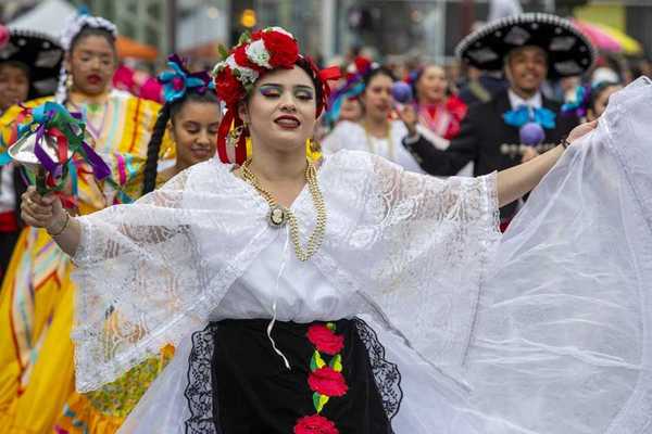 A woman in a traditional Mexican outfit with others in similar clothing parading behind her