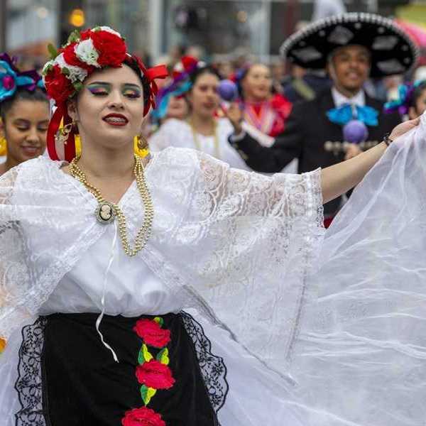 A woman in a traditional Mexican outfit with others in similar clothing parading behind her