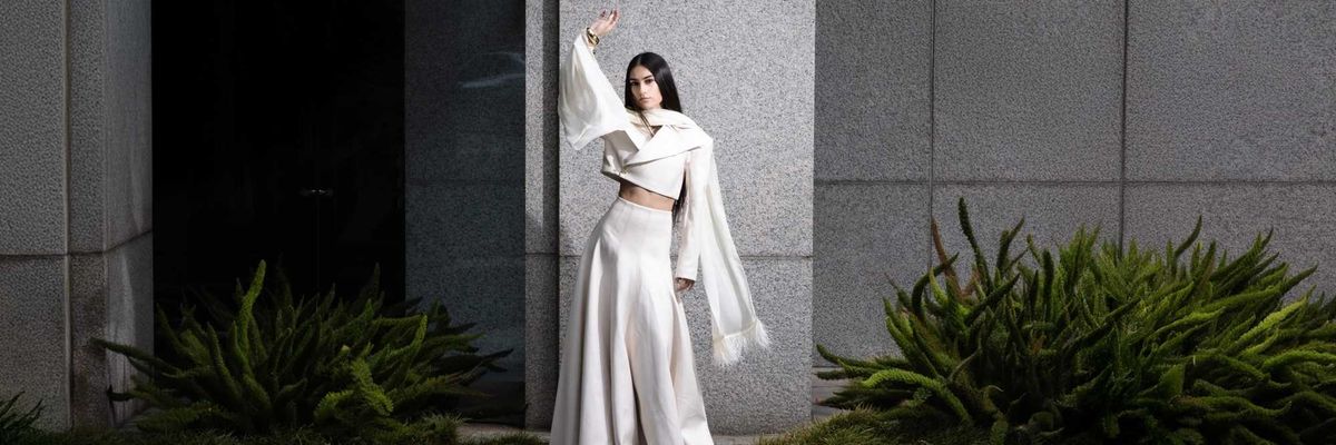 A woman in a voluminous white skirt and blazer posing by a pond