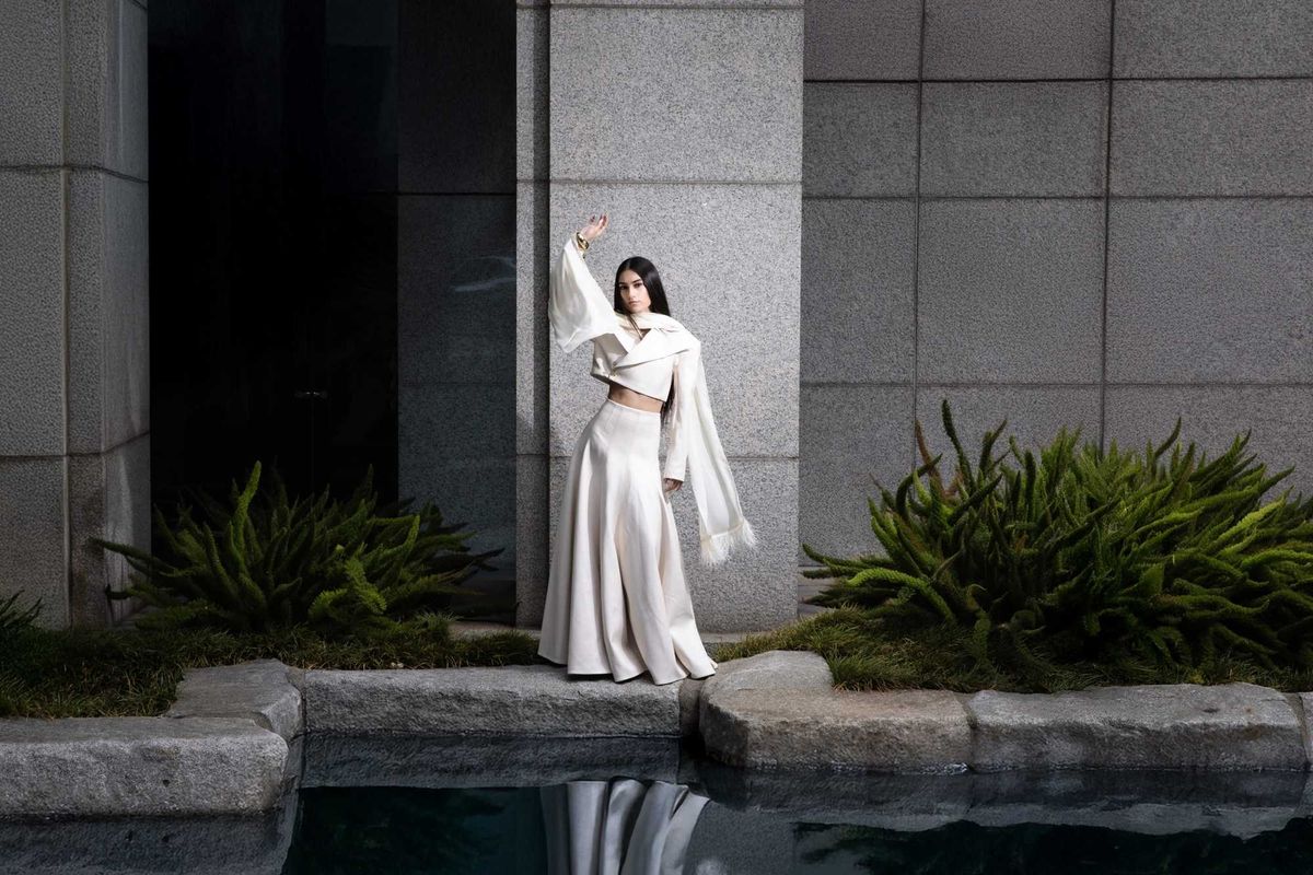 A woman in a voluminous white skirt and blazer posing by a pond