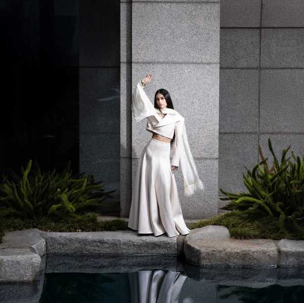 A woman in a voluminous white skirt and blazer posing by a pond