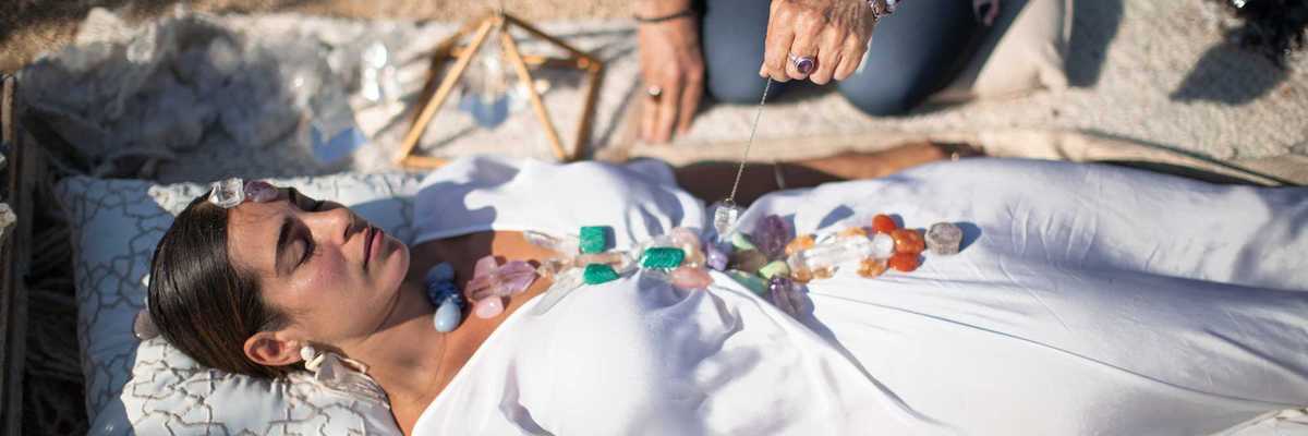 a woman in a white dress with stones on her and a healer kneeling over her