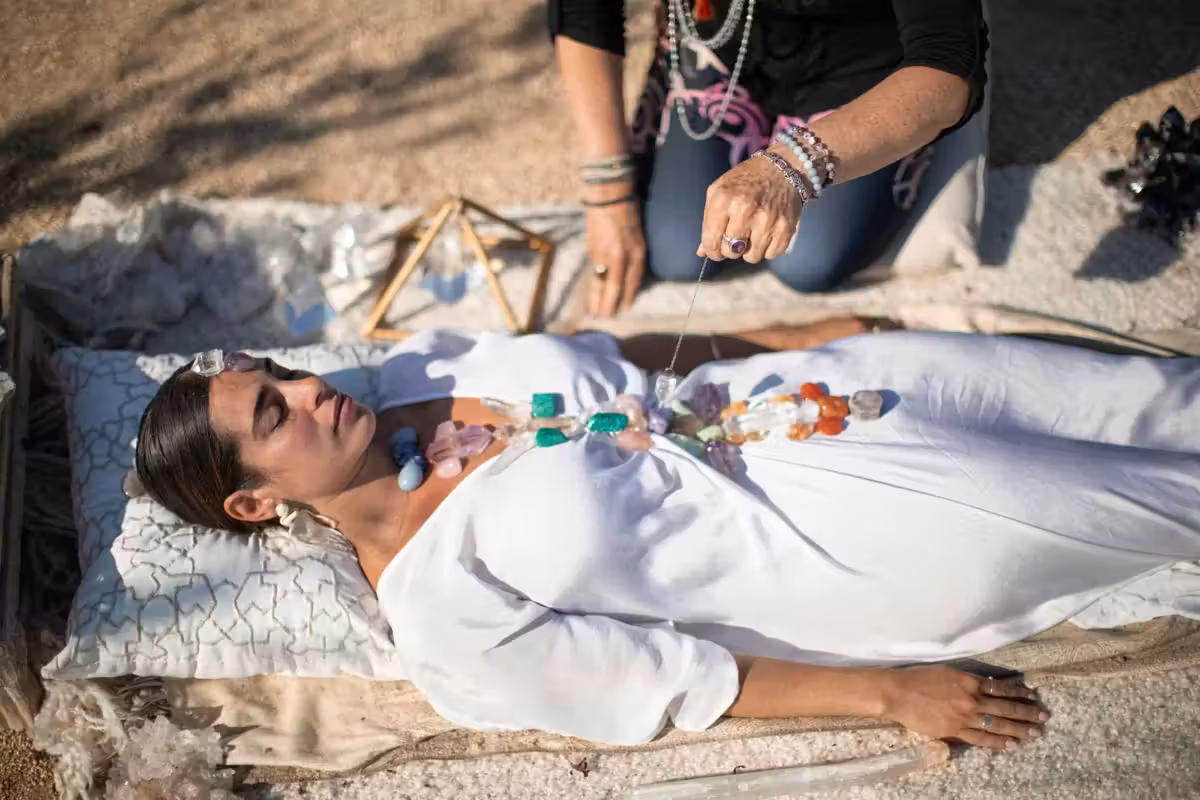 a woman in a white dress with stones on her and a healer kneeling over her