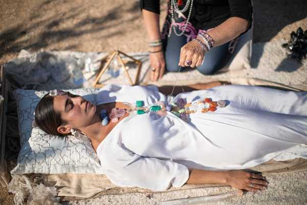 a woman in a white dress with stones on her and a healer kneeling over her