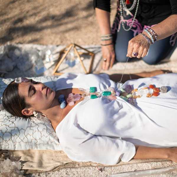 a woman in a white dress with stones on her and a healer kneeling over her