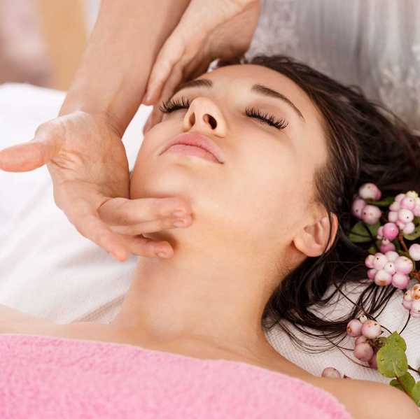 a woman laying on a treatment bed getting a facial with a sprig of berries next to her