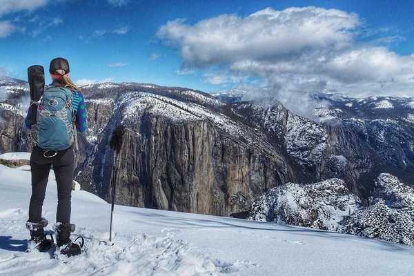 A woman looking out at Yosemite Valley from a snowy trail in snowshoes