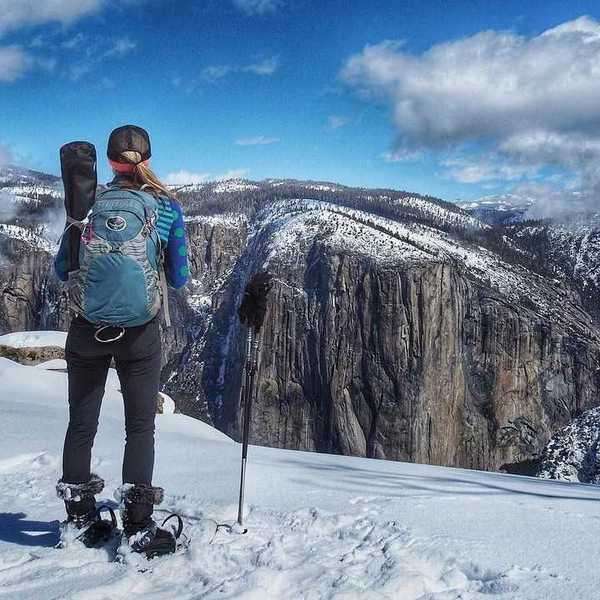 A woman looking out at Yosemite Valley from a snowy trail in snowshoes