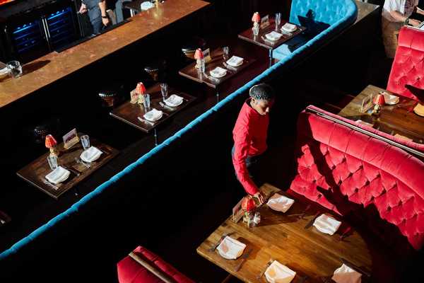 a woman setting a table in a restaurant with large red velvet booths