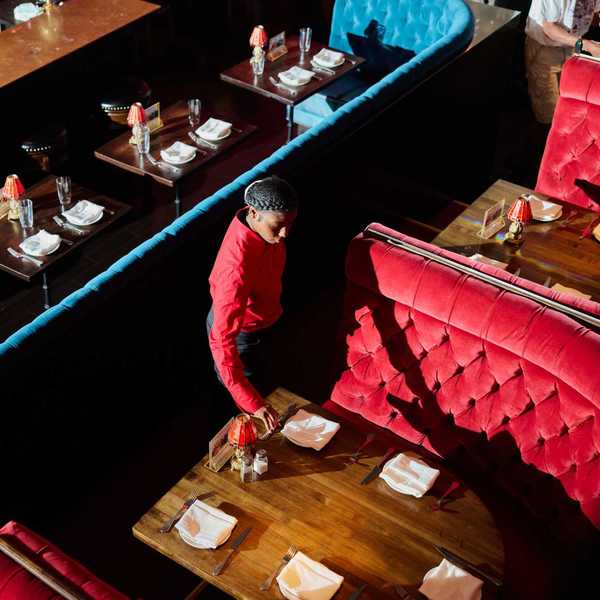 a woman setting a table in a restaurant with large red velvet booths