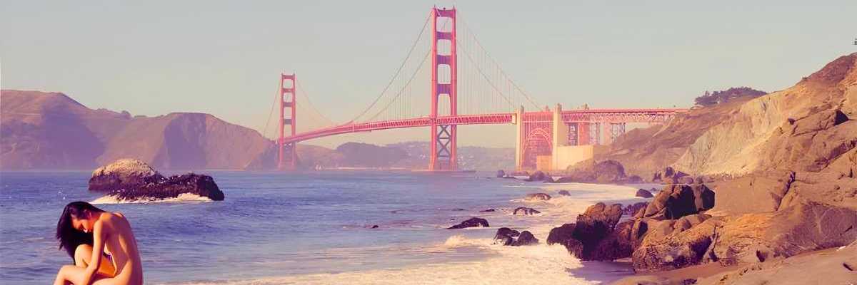 a woman sitting on a rock at the beach in front of the golden gate bridge