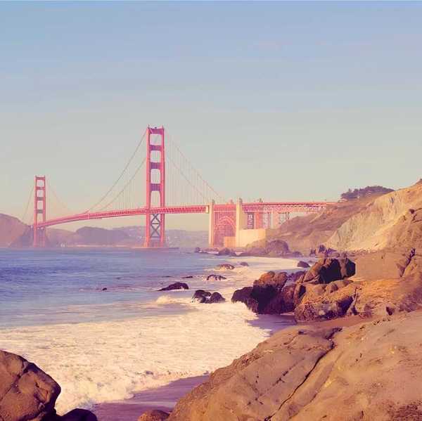 a woman sitting on a rock at the beach in front of the golden gate bridge