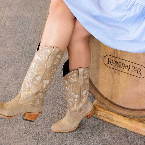 a woman sitting on a Rombauer Vineyards wine barrel wearing a pair of champagne colored cowboy boots with a floral design
