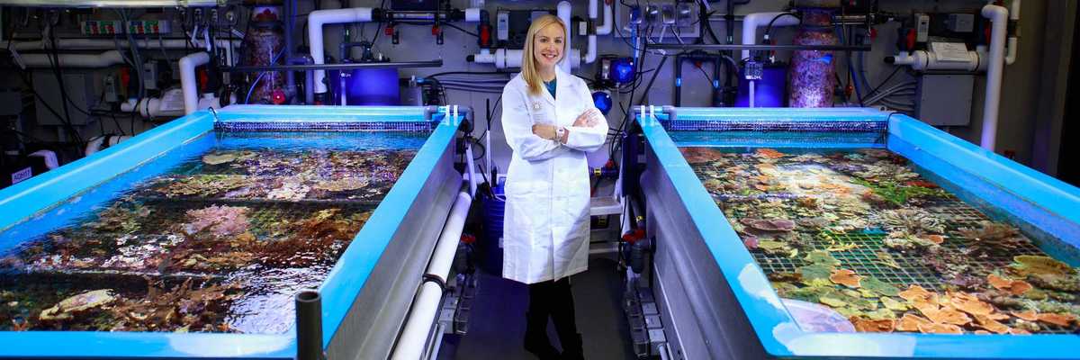 a woman standing in a lab with coral in tanks