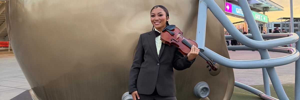 a woman with a violin standing in front of a giant football helmet that says LX Super Bowl