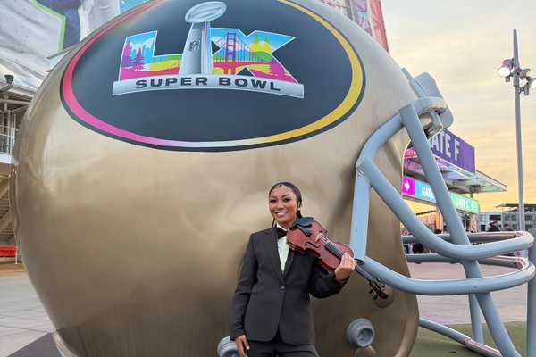 a woman with a violin standing in front of a giant football helmet that says LX Super Bowl