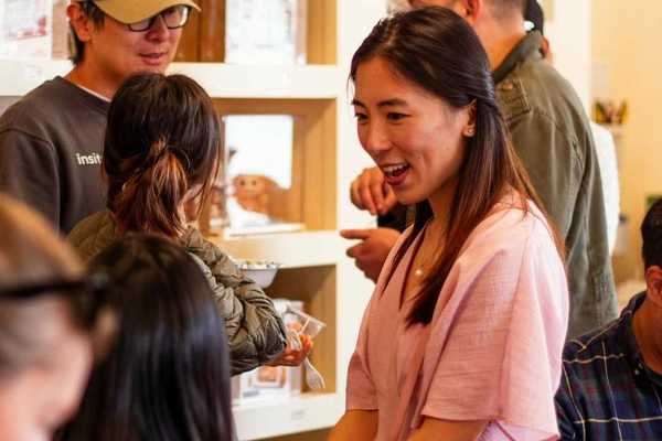 a women with straight dark hair in a pink dress talking to people in a store