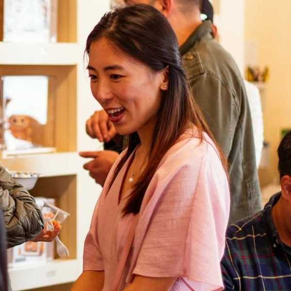 a women with straight dark hair in a pink dress talking to people in a store