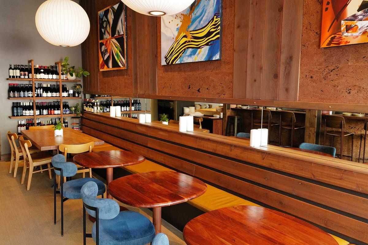 a wood paneled dining room with small round tables and a wall of wine bottles