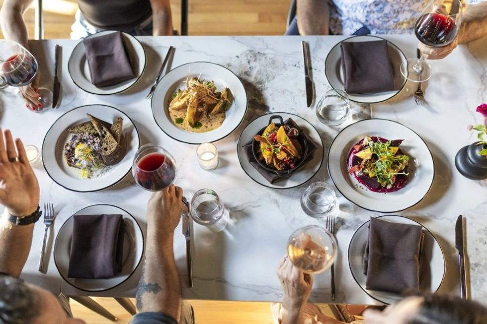Aerial view of a dining table with gourmet dishes, red wine, and place settings.