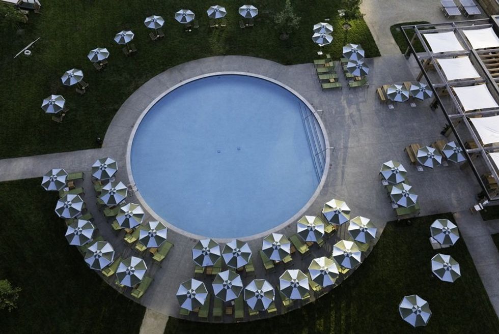Aerial view of an empty circular pool surrounded by umbrellas and lounge chairs.