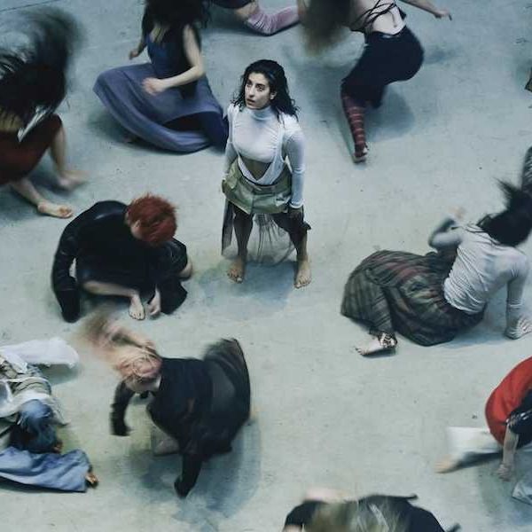 Aerial view of dancers in motion, surrounding one standing still, with blurred dynamic movements.