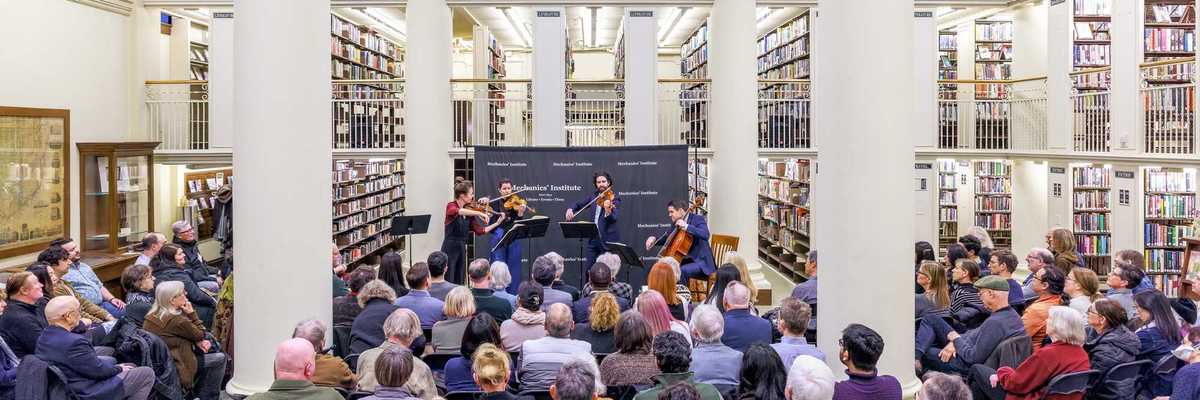 an audience sitting in a library listening to a quartet of musicians