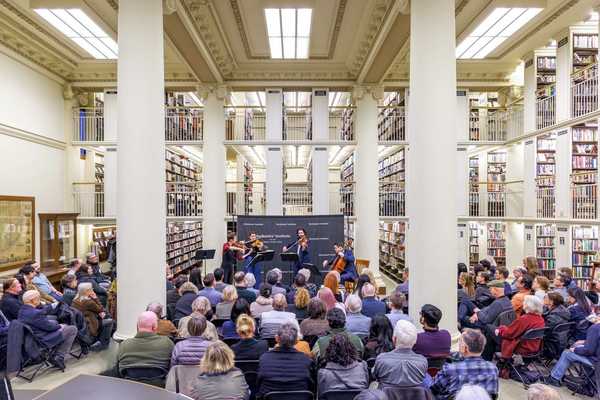 an audience sitting in a library listening to a quartet of musicians