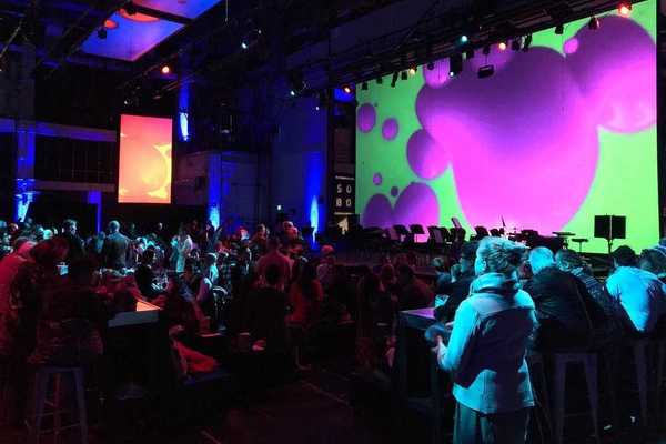 an auditorium full of people with a screen with colorful imagery