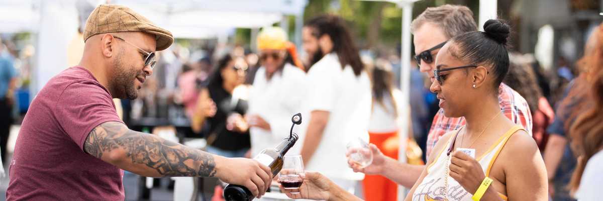 an outdoor event where wine is being poured for someone in line at a table