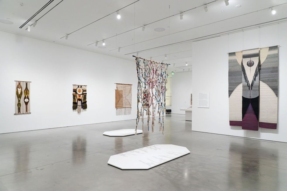 Art gallery with colorful hanging textiles on white walls.