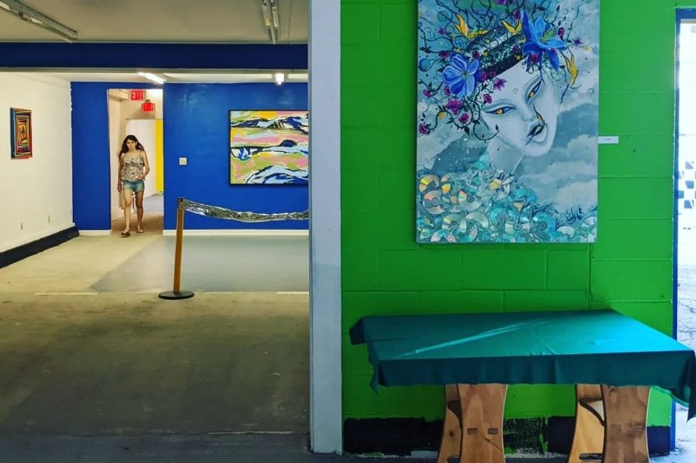 Art gallery with colorful paintings on vibrant walls, woman walking in the distance.