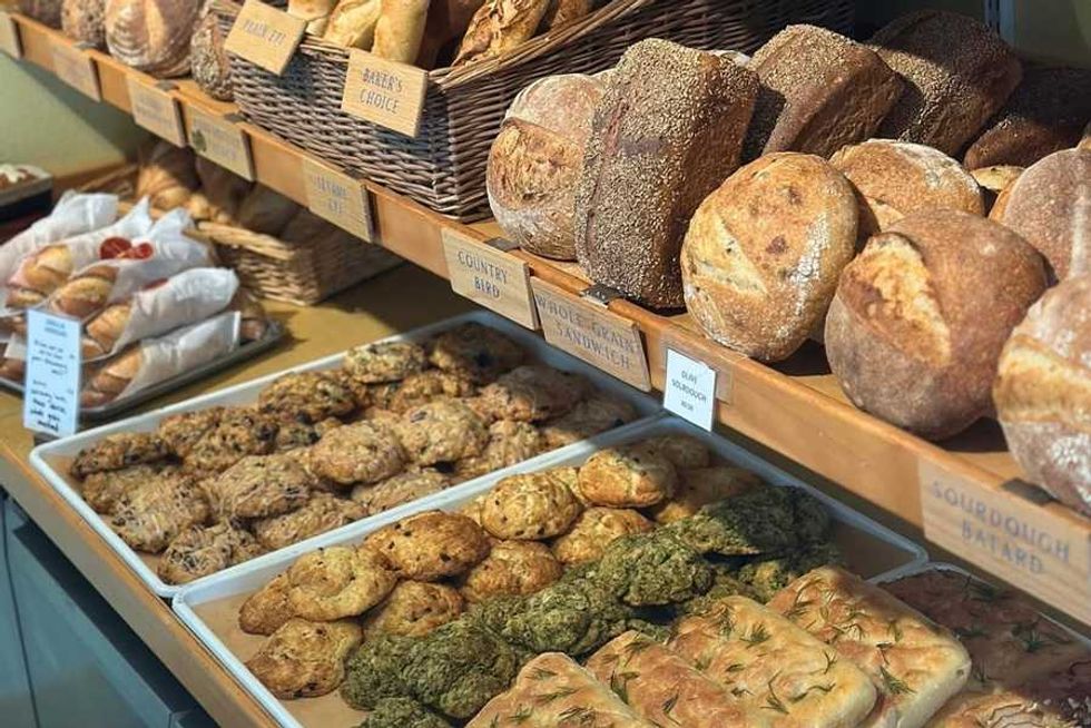 Assorted breads and pastries displayed on wooden shelves and trays in a bakery.
