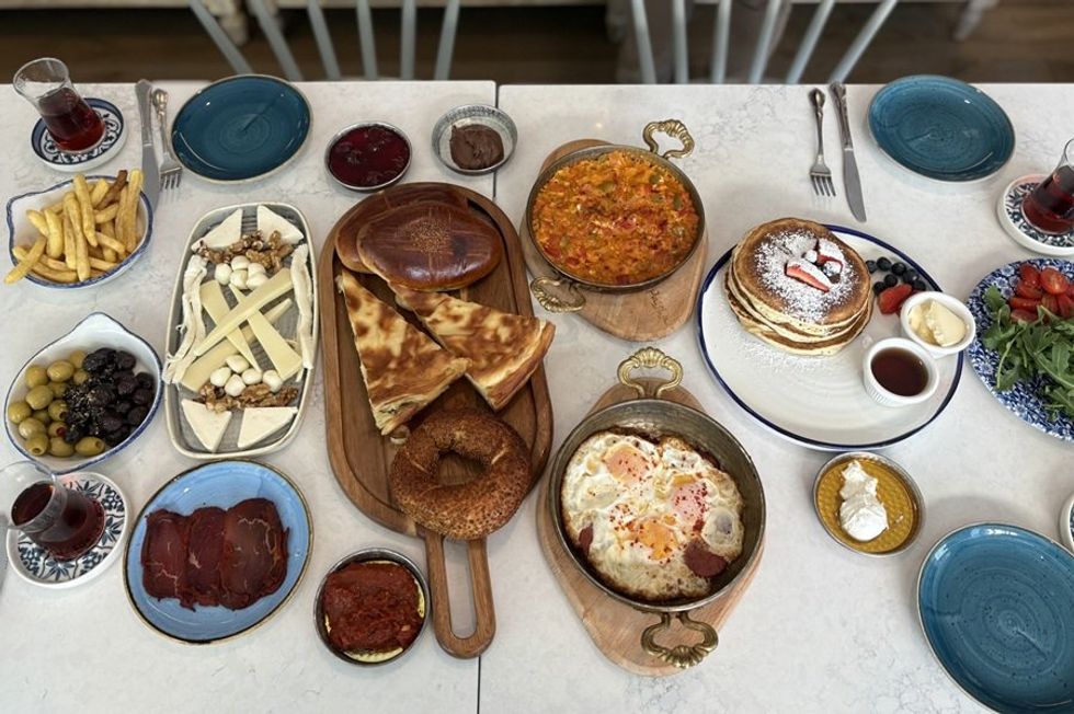 Assorted breakfast spread with pastries, pancakes, eggs, and various sides on a table.