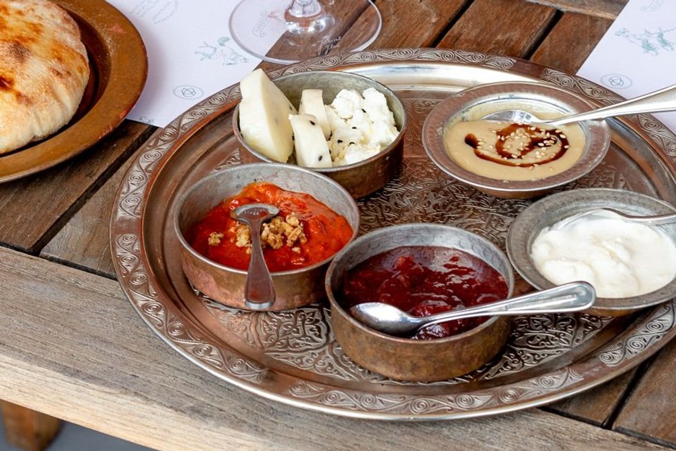 Assorted dips and cheeses on a decorative tray next to flatbread on a wooden table.
