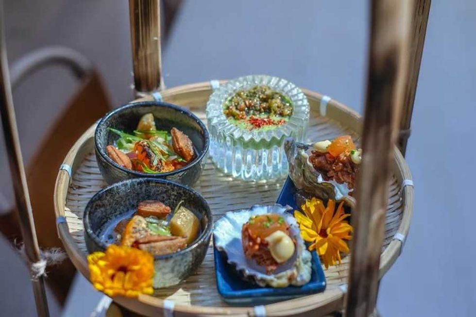 Assorted gourmet appetizers on a round bamboo tray, garnished with flowers.