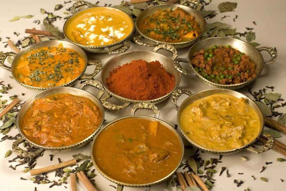 Assorted Indian curries and spices in small brass bowls, surrounded by whole spices.