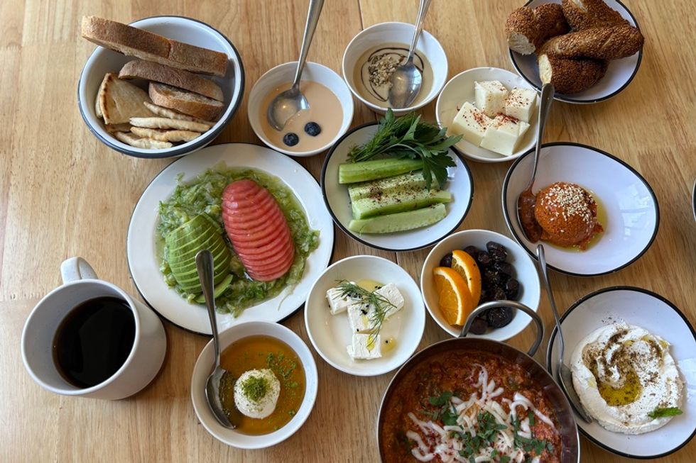 Assorted Mediterranean breakfast items on a table with coffee, bread, veggies, and spreads.