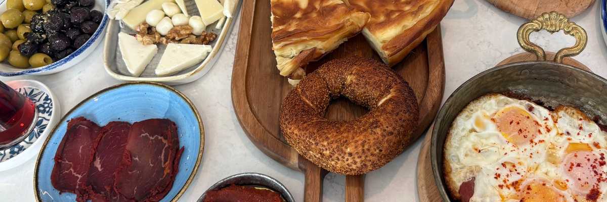 Assorted Turkish breakfast spread with breads, cheeses, olives, tea, and fried eggs.