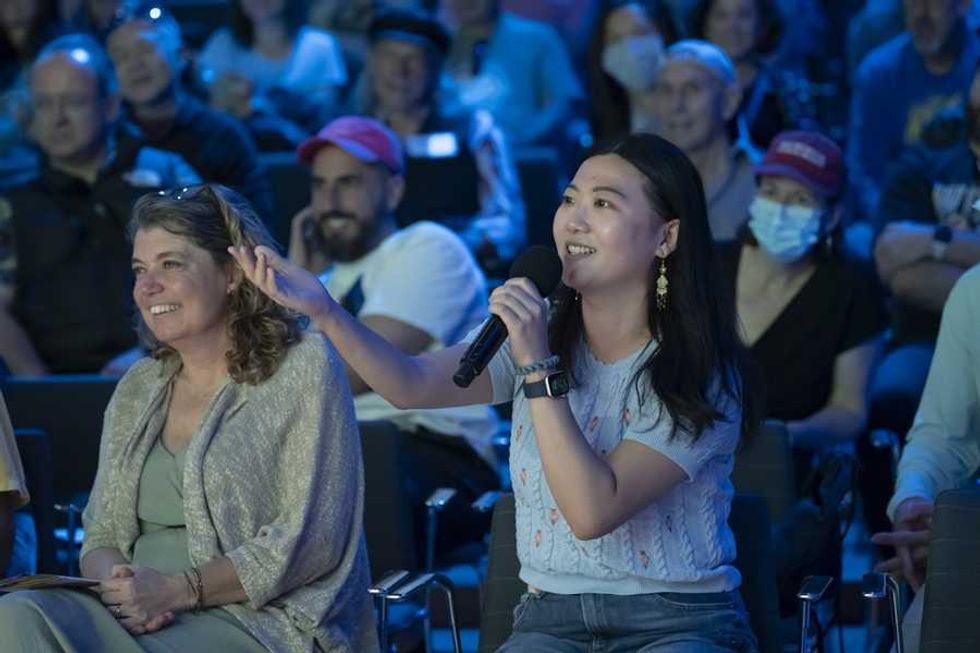 Audience member asking a question with a microphone at an indoor event.